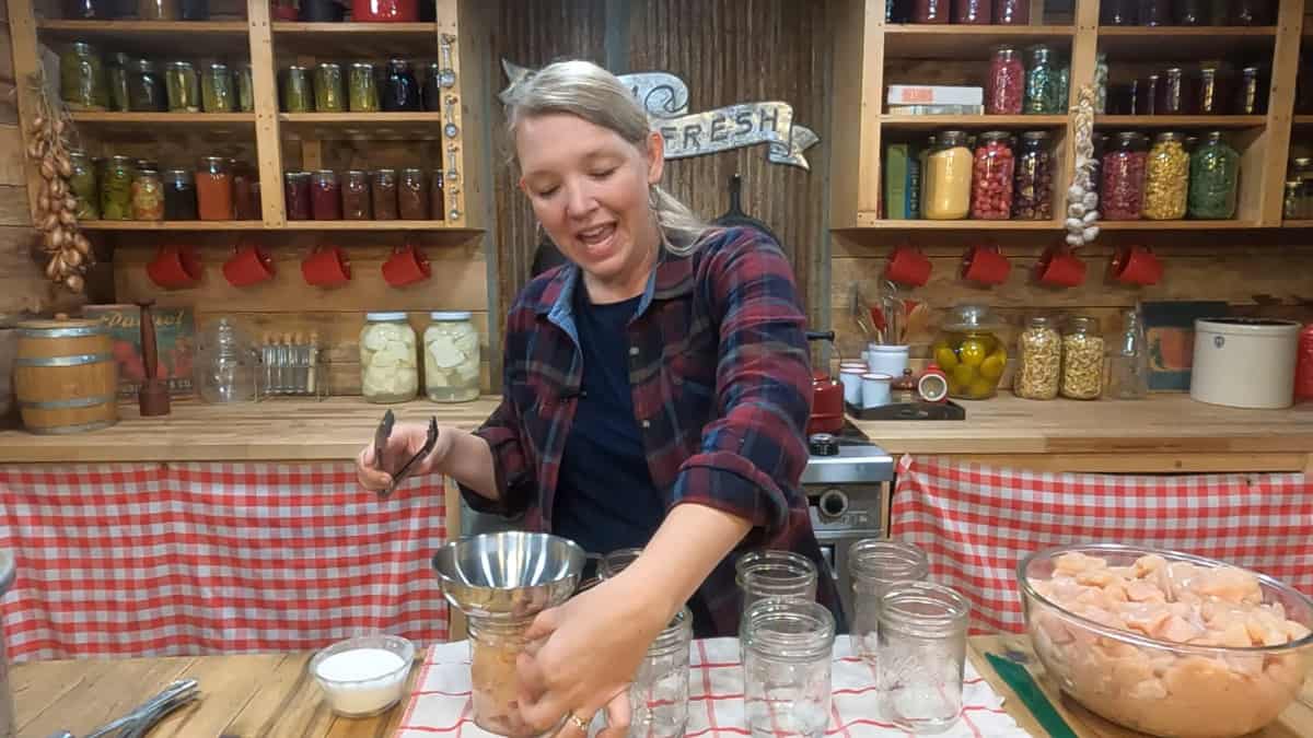 A woman adding raw chicken to Mason jars.