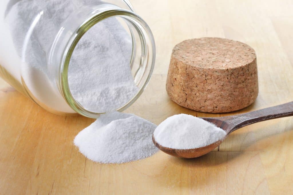 A jar of baking soda tipped onto a table with a spoonful next to it.