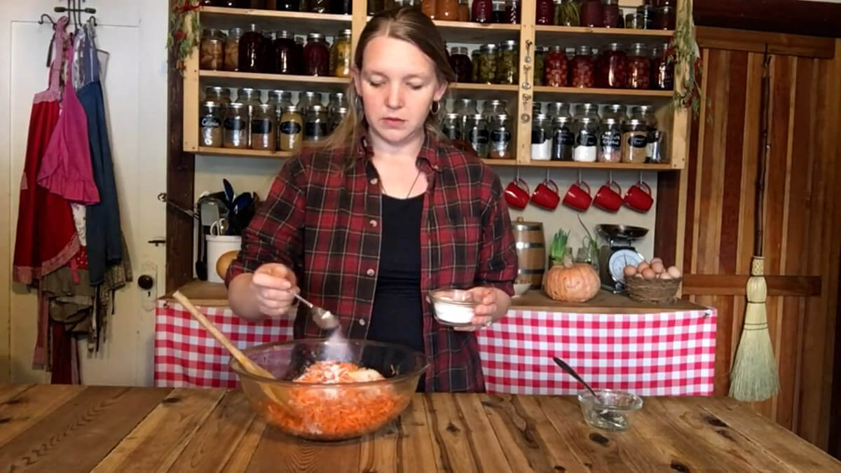 A woman mixing carrots, salt, ginger, and starter liquid in a large bowl to make fermented carrots.