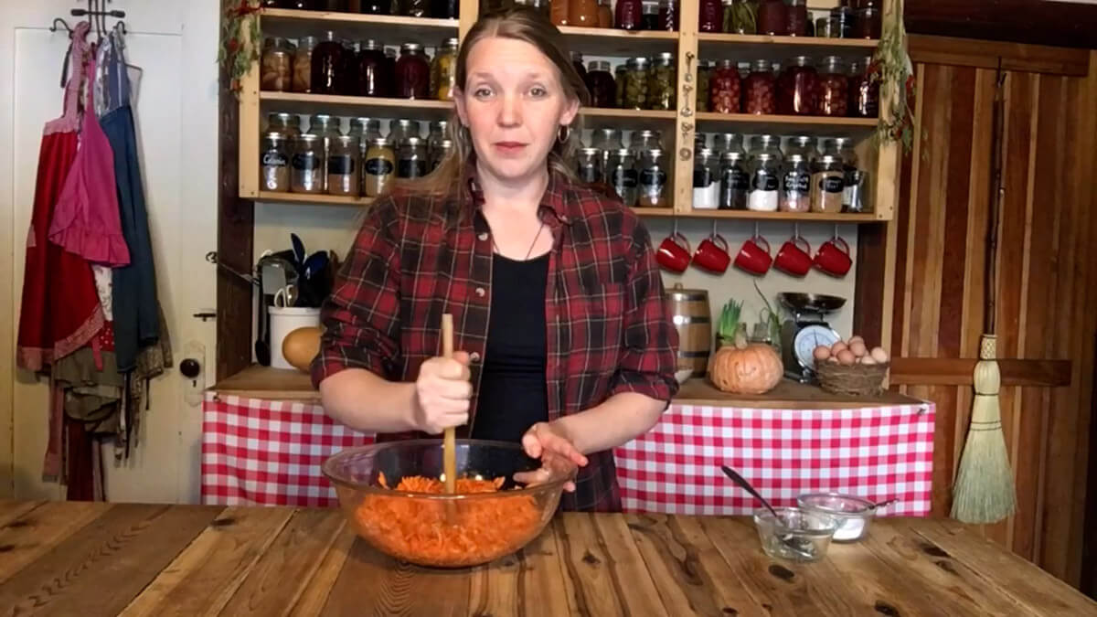 A woman pounding carrots, salt, ginger, and starter liquid in a large bowl to make fermented carrots.