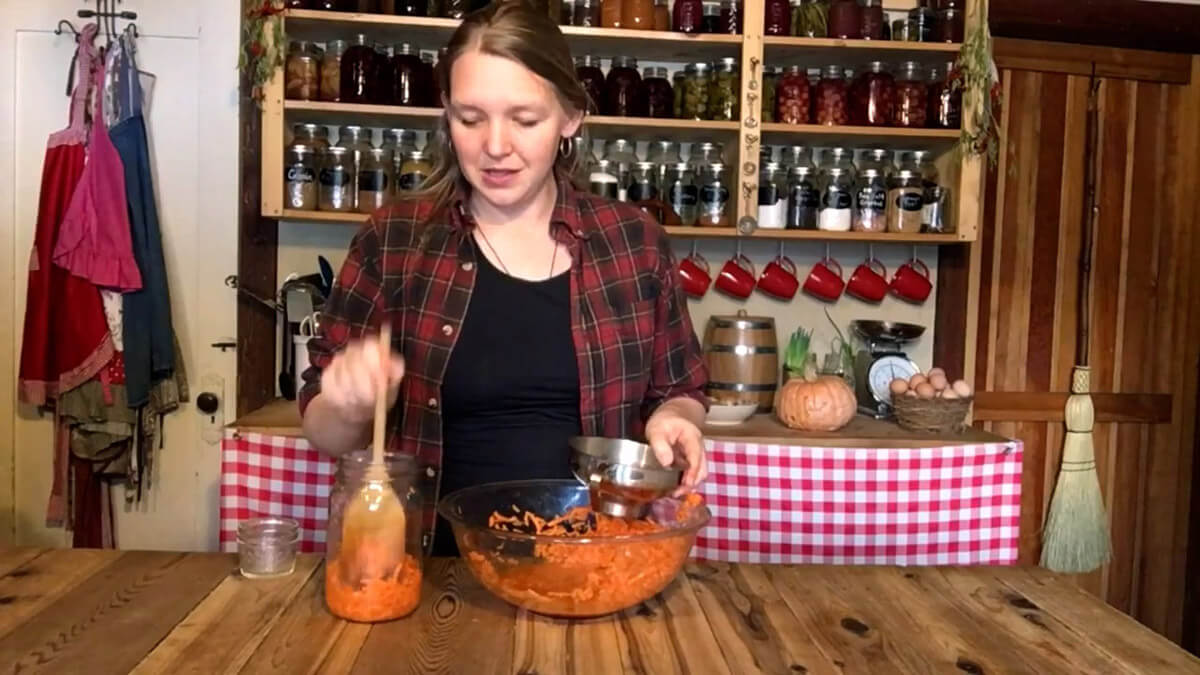 A woman transferring carrot mixture from a large bowl into a quart jar to make fermented carrots.