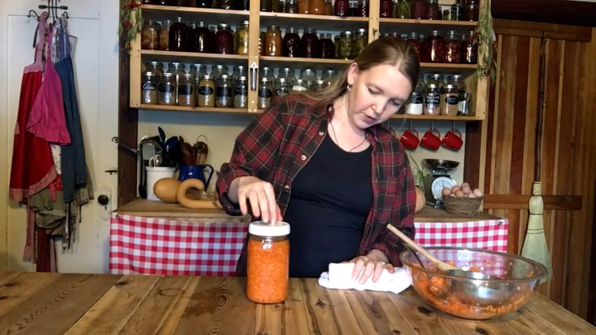 A woman placing a lid on a jar of carrots ready to ferment.