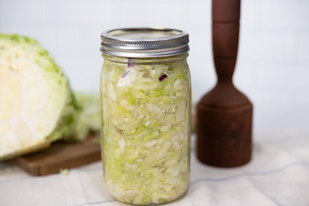 A jar of fermented sauerkraut sitting next to a kraut pounder.