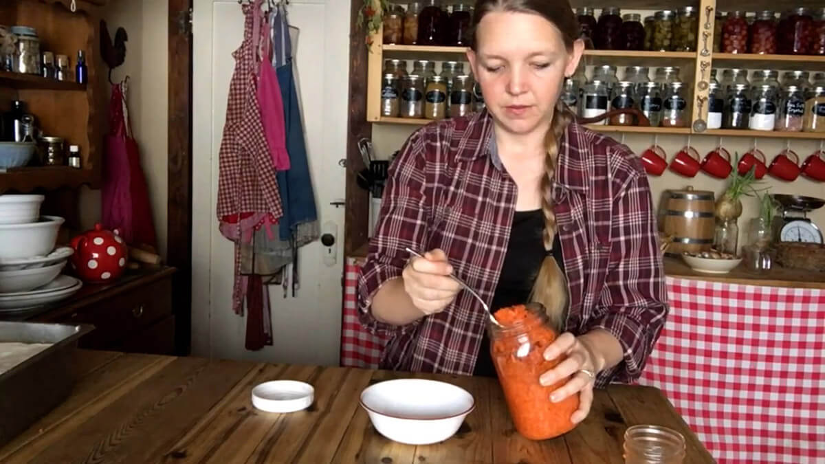 A woman dishing finished fermented carrots out of a jar.