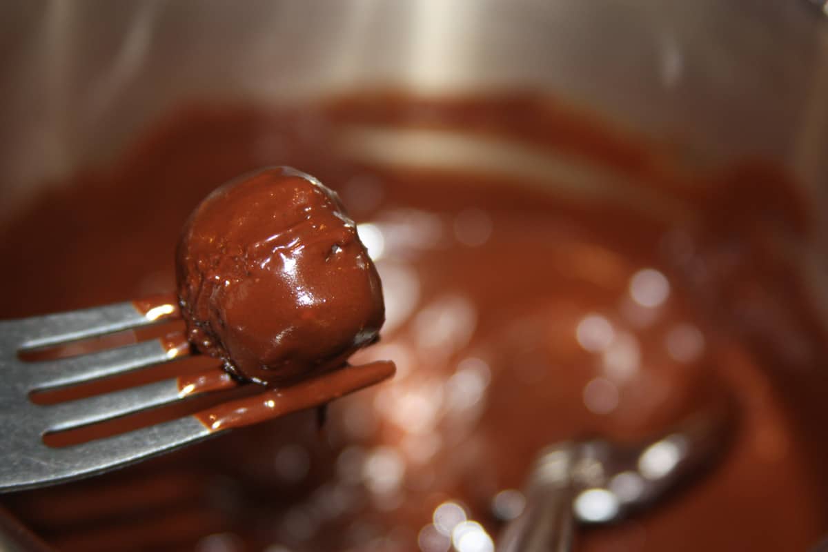 Coconut truffle getting dipped in chocolate.