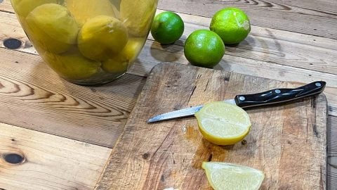 Sliced fermented limes on a cutting board with crock in background.