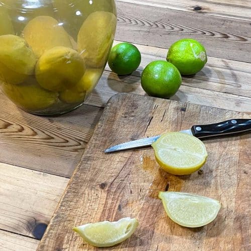 Sliced fermented limes on a cutting board with crock in background.