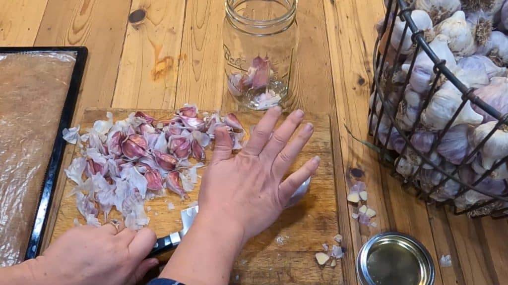 Hands smashing garlic cloves with a knife.
