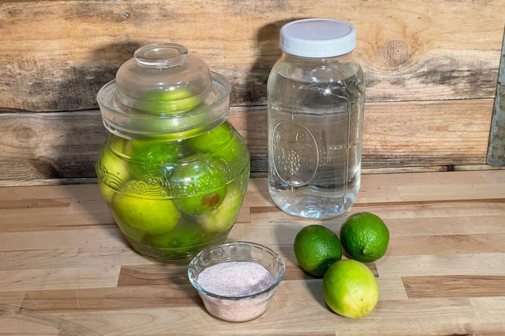 Fermenting limes in a crock next to the ingredients needed to ferment limes.