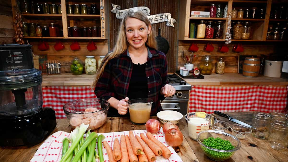 A woman in the kitchen with chicken pot pie ingredients on the counter in front of her.