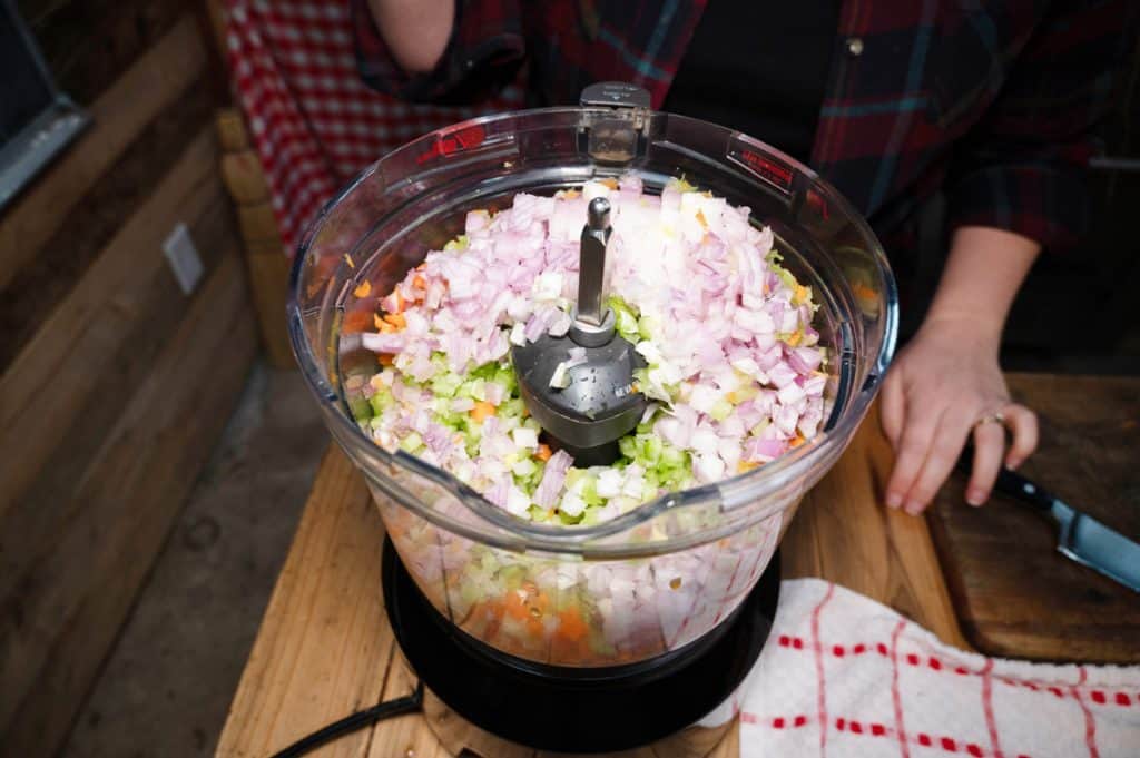 A food processor filled with chopped carrots, celery and onions.