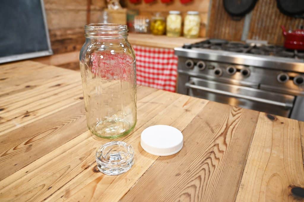 A half-gallon wide-mouth mason jar with lid and fermentation weight sitting on a wooden counter.
