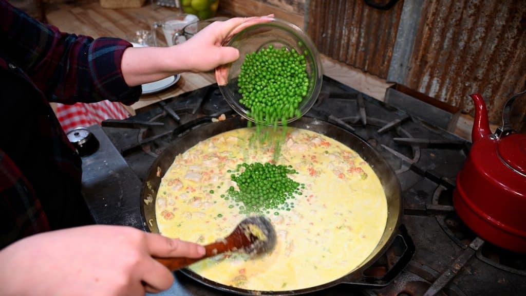 Peas being added to a skillet filled with chicken pot pie filling.