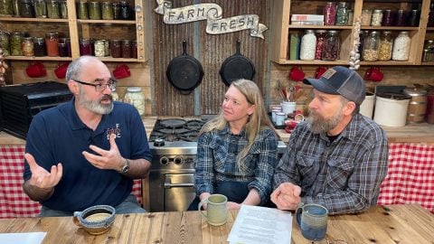 Three people sitting behind a kitchen counter talking.