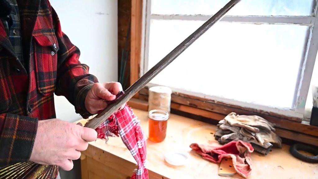 A man oiling the long wooden handle of a garden tool.