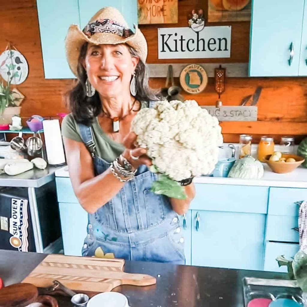 A woman in a cowboy hat holding up a large head of cauliflower.