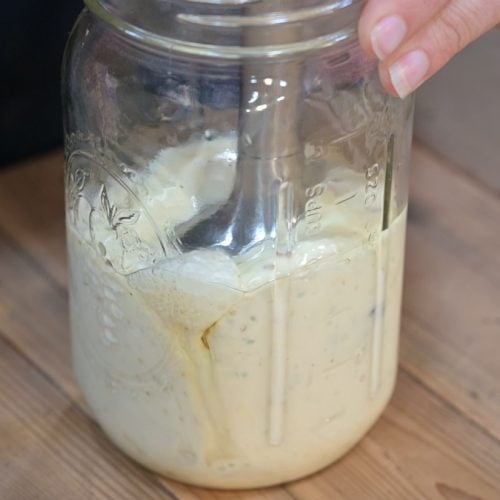 A quart jar of mayo being blended with an immersion blender.