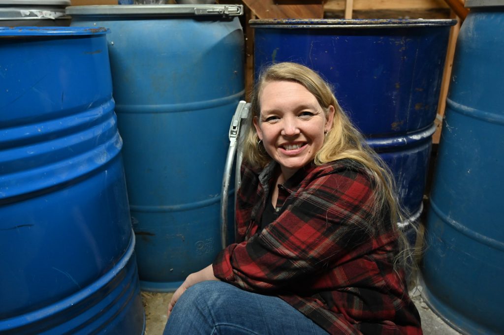 A woman sitting beside 55 gallon food-grade barrels.