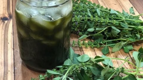 A glass of instant iced tea on a counter with fresh herbs.