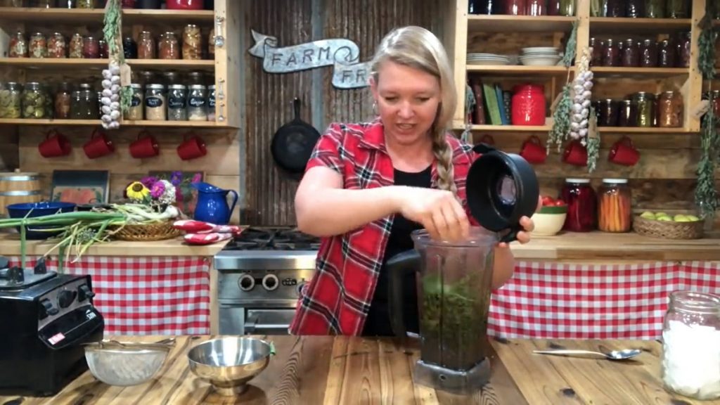 A woman putting herbs into a blender with water.
