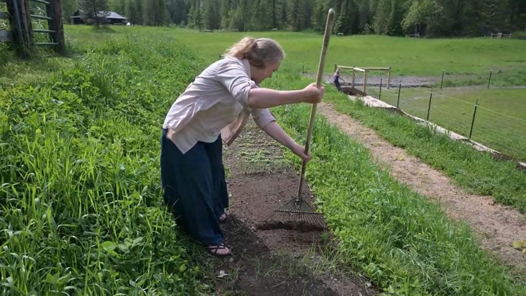 A woman preparing a garden bed with a rake.