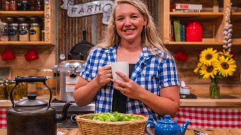 A woman with a cup in her hand and a basket of hops in front of her.