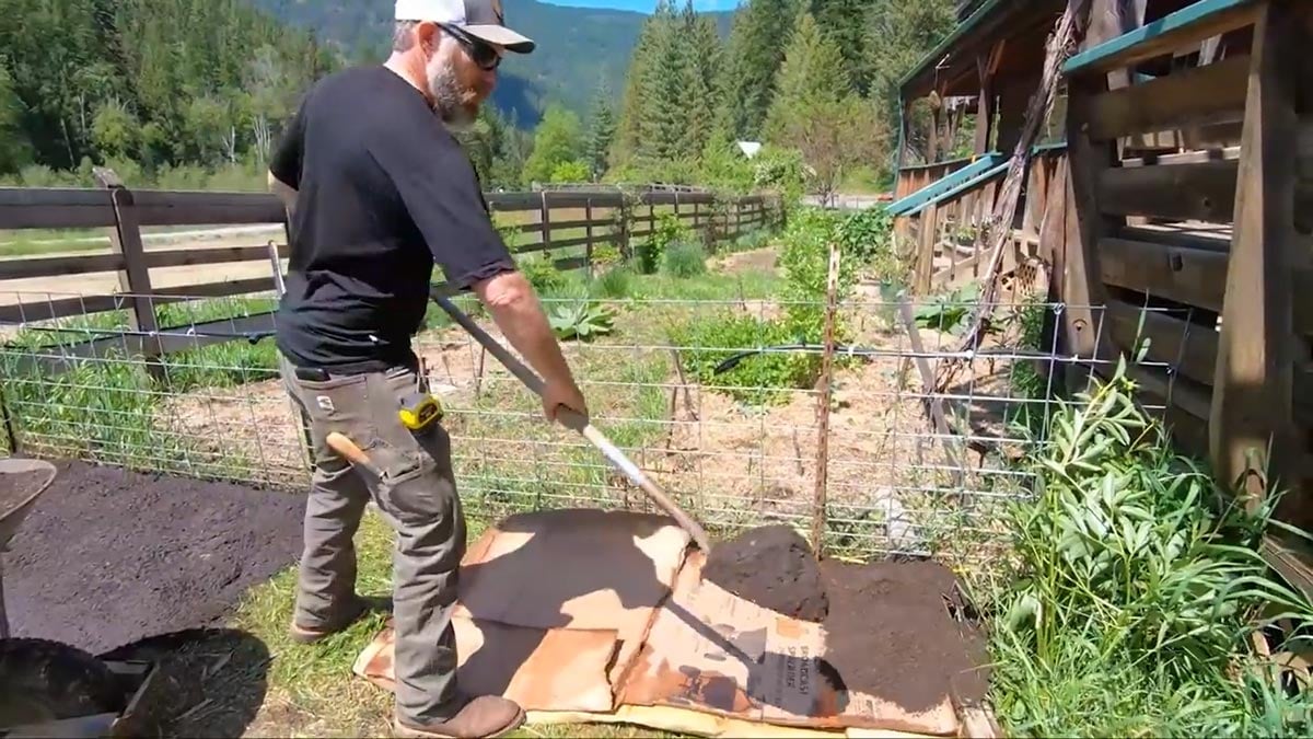 A man shoveling soil onto cardboard.