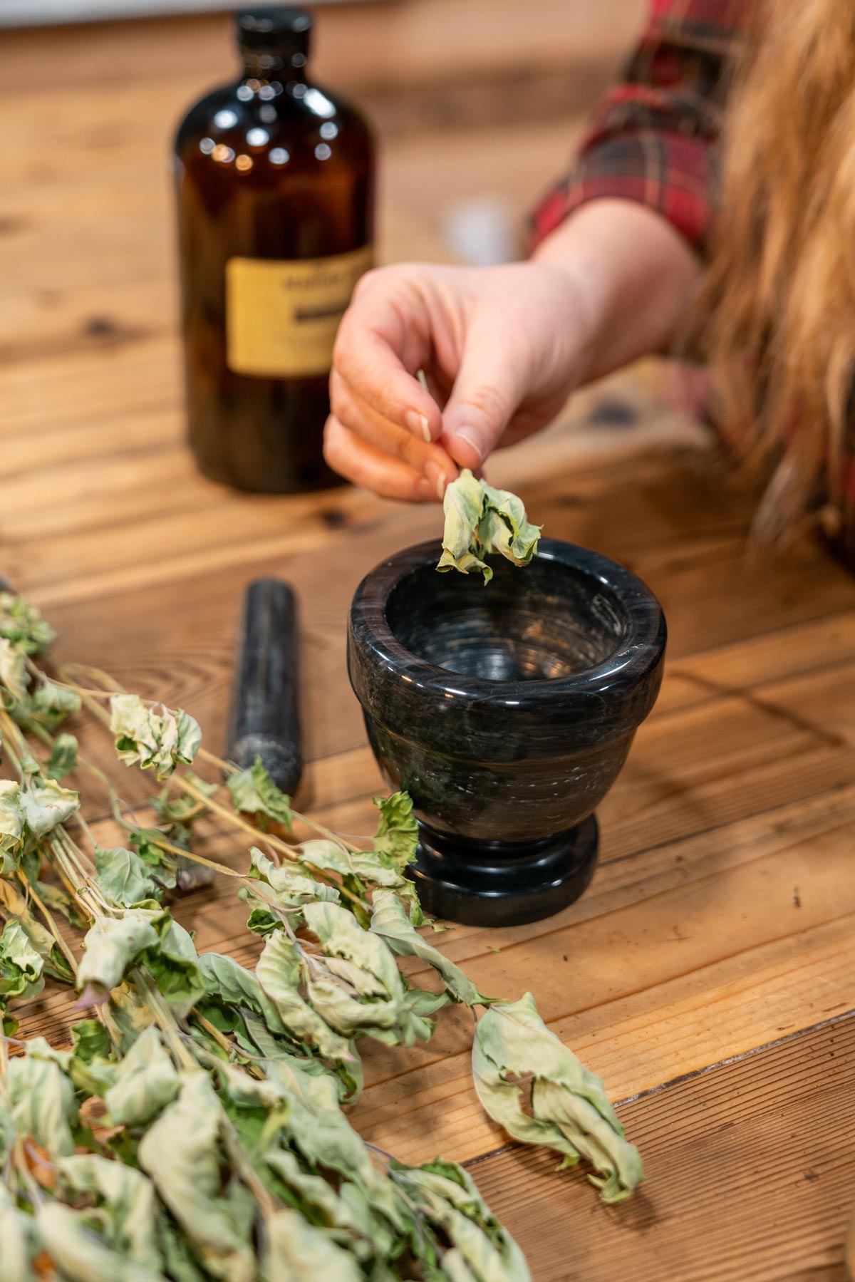 A woman's hand putting dried herbs into a mortar.