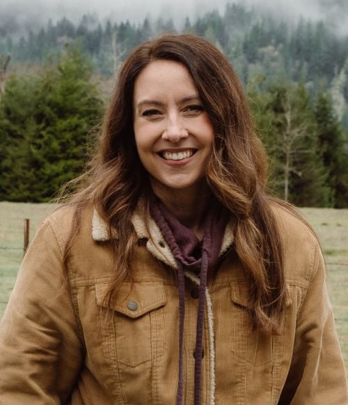 A woman in a jacket standing in front of a field and mountain.