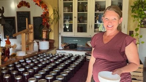 A woman standing beside dozens of jars of plum jelly.