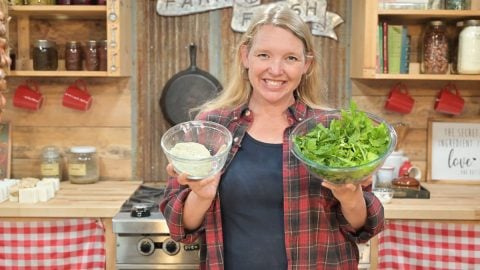 A woman holding a bowl of celery salt and a bowl of celery leaves.