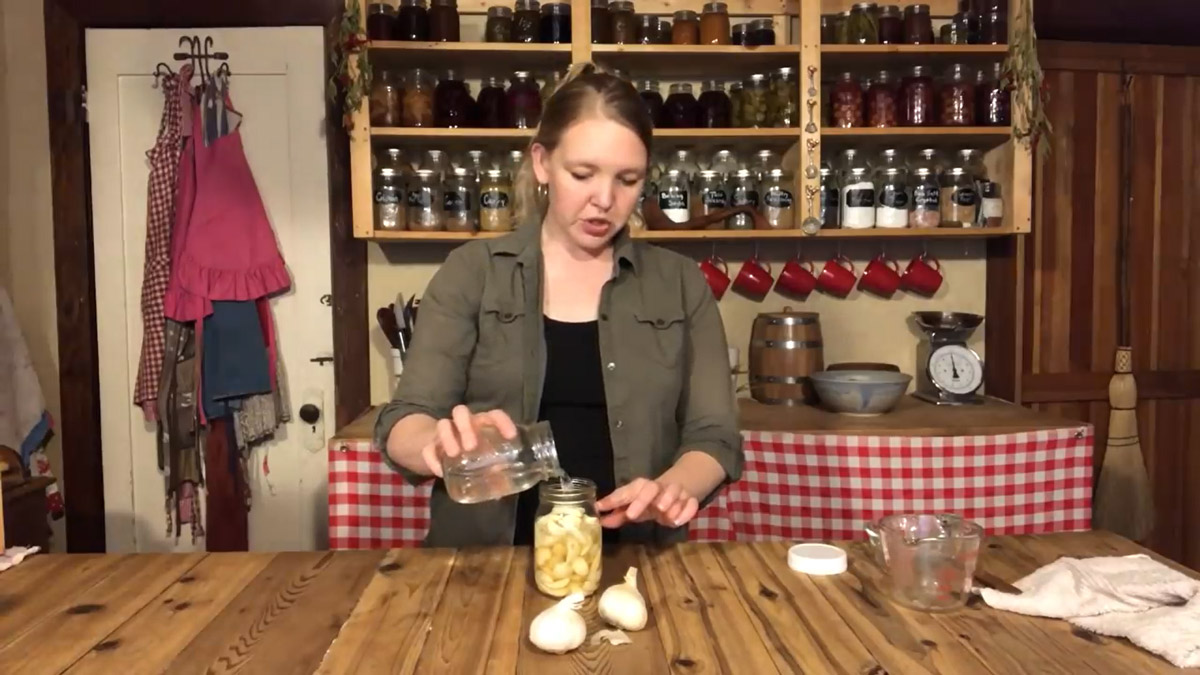 A woman pouring brine into a jar of garlic.
