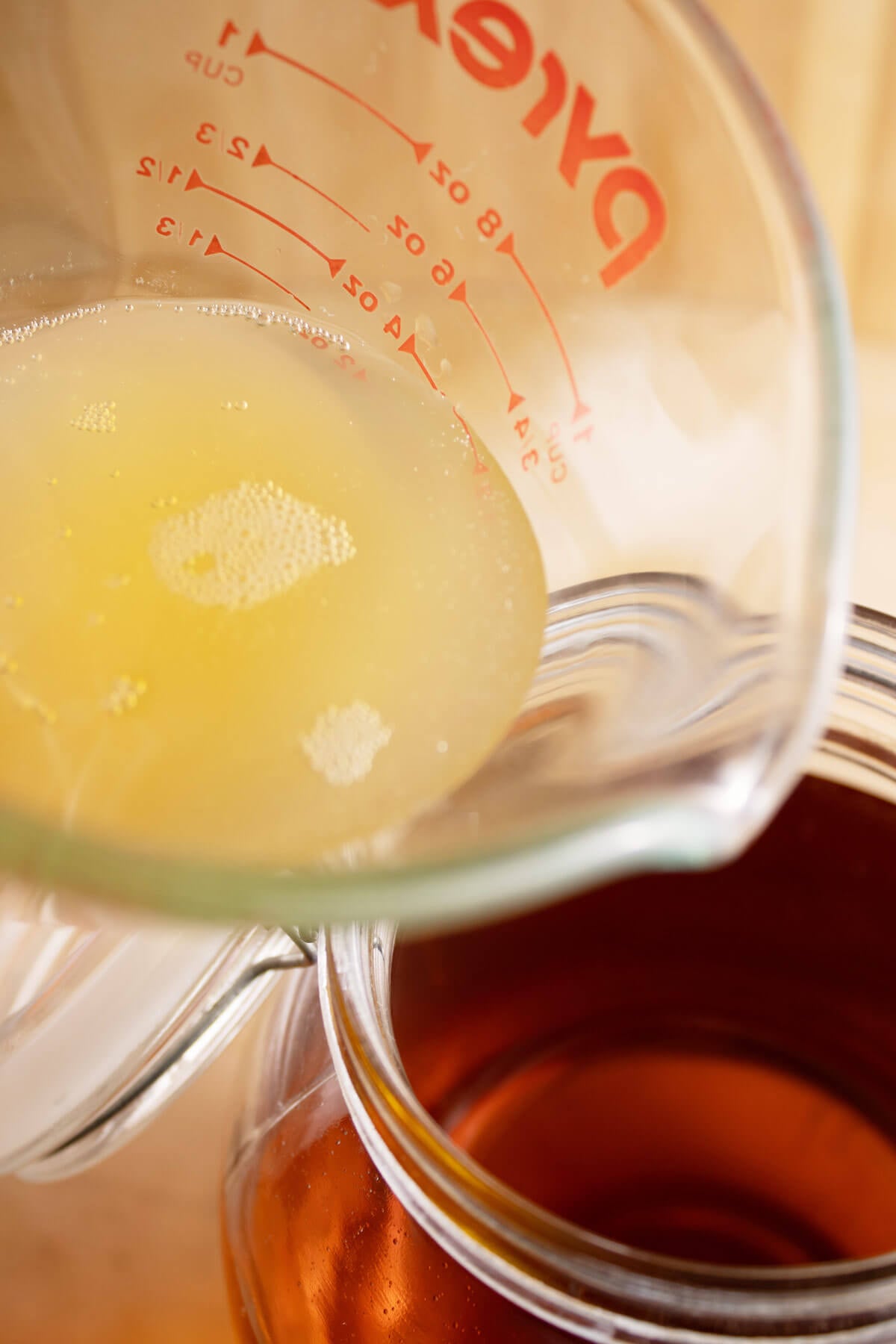 Pouring kombucha from a measuring cup into a gallon jar filled with apple cider.