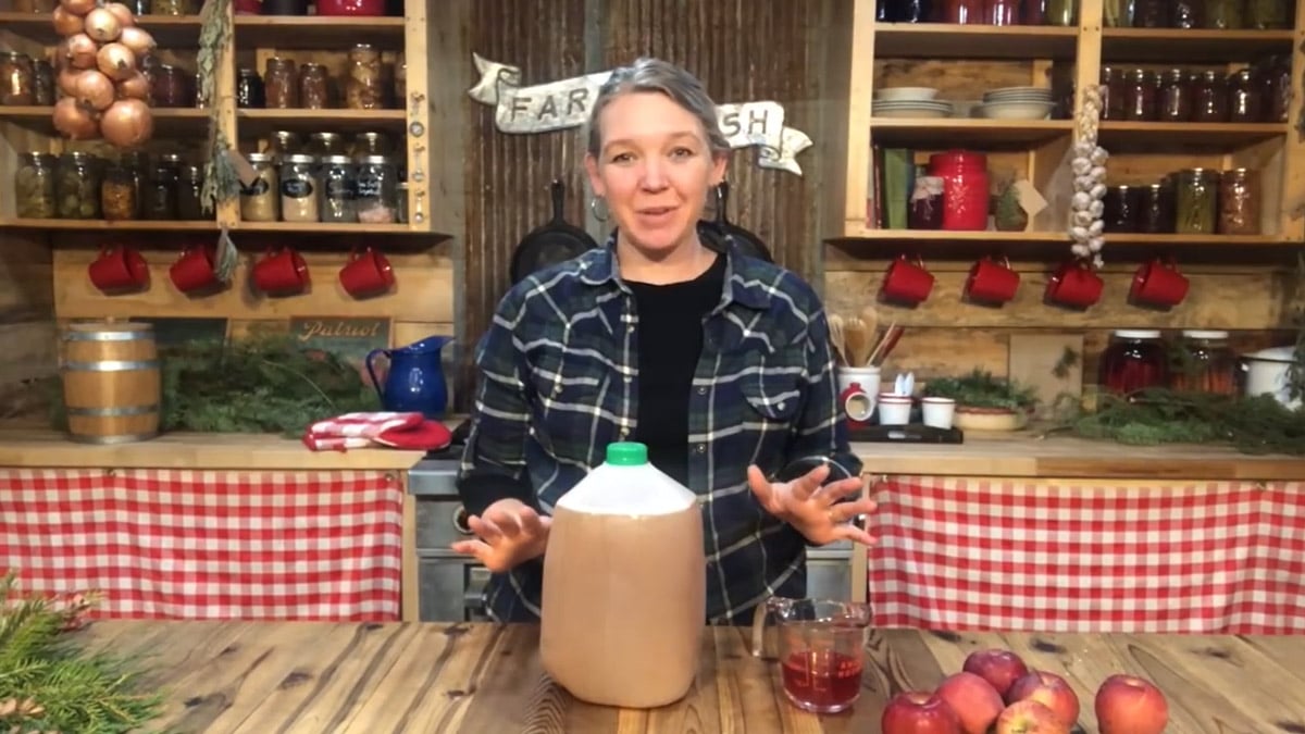 A woman standing in front of a jug of sparkling apple cider.
