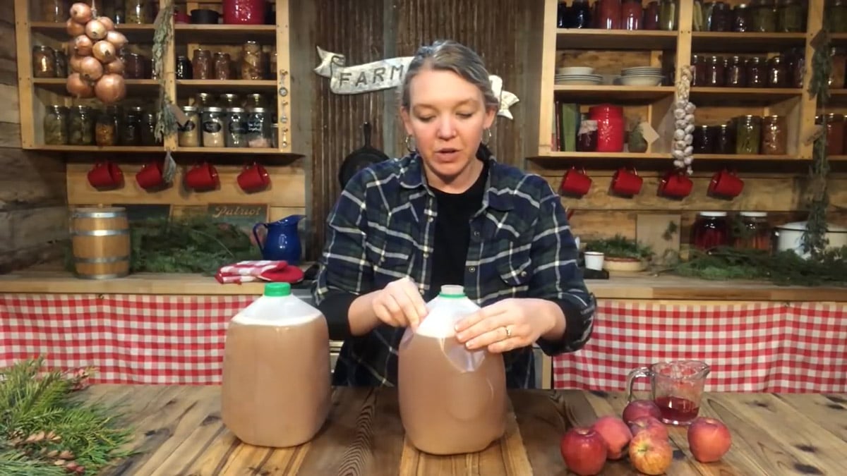 A woman pressing in the sides of a jug of sparkling apple cider to allow for expansion.