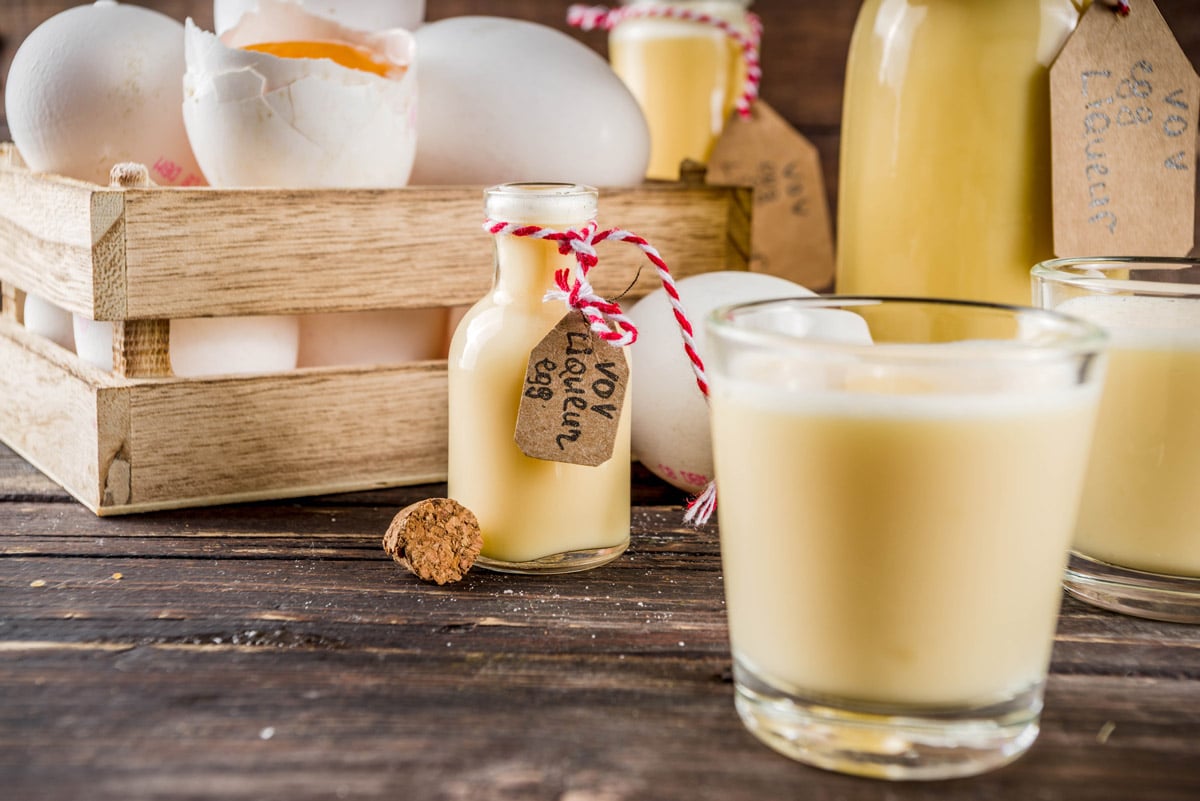 Aged eggnog in a glass with a bottle in the background.