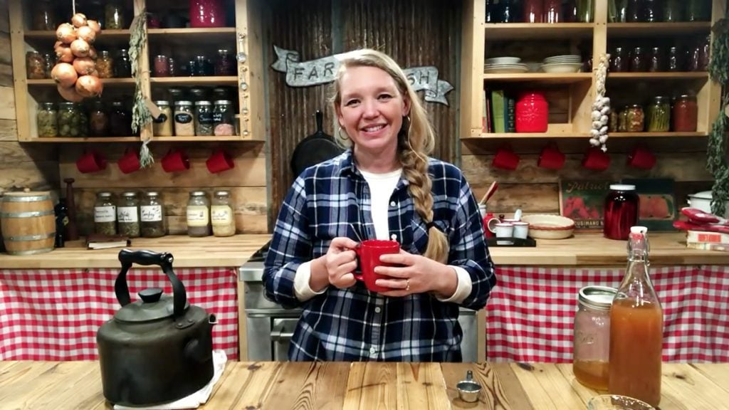 A woman holding a cup of tea standing in the kitchen.