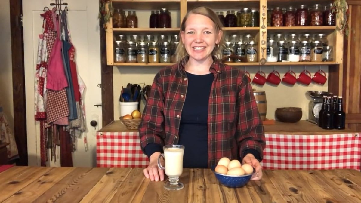 A woman standing in the kitchen with a bowl of eggs and a glass of homemade eggnog.