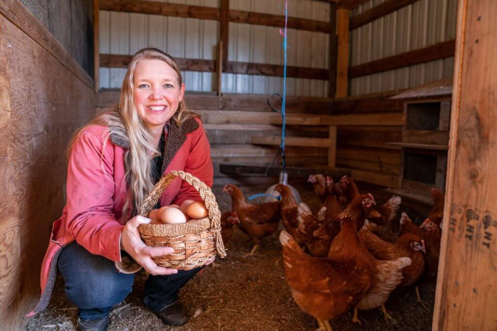 A woman in a chicken coop holding a basket of eggs.