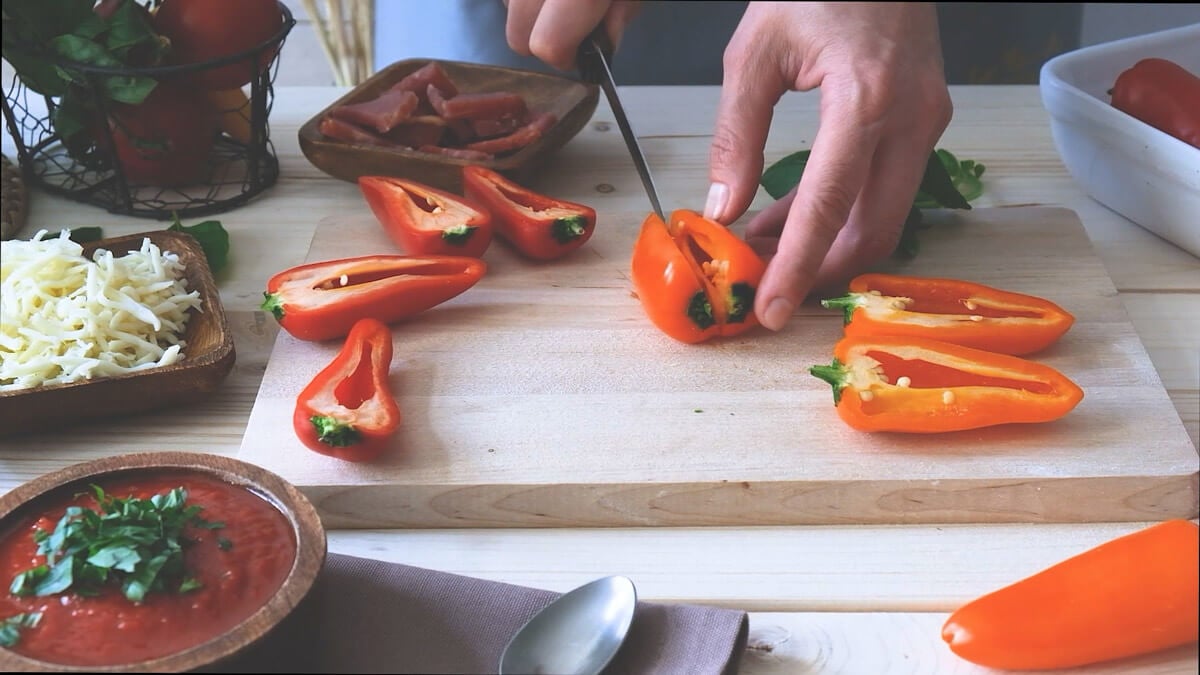 Hands cutting peppers in half to prepare for bell pepper pizzas.