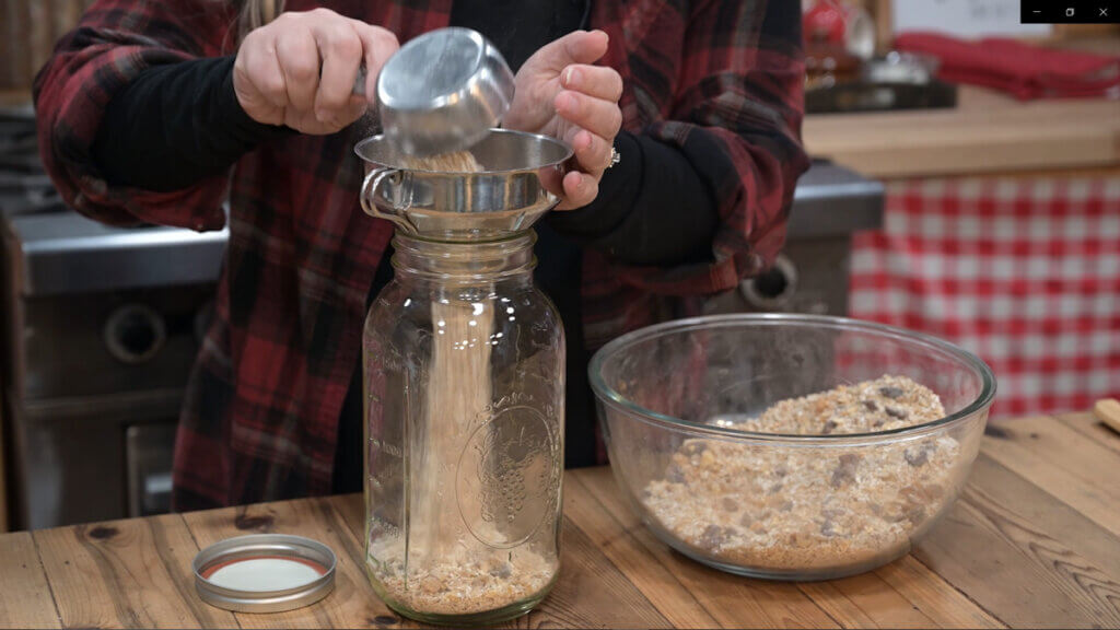 A woman's hands pouring instant breakfast into a large Mason jar.