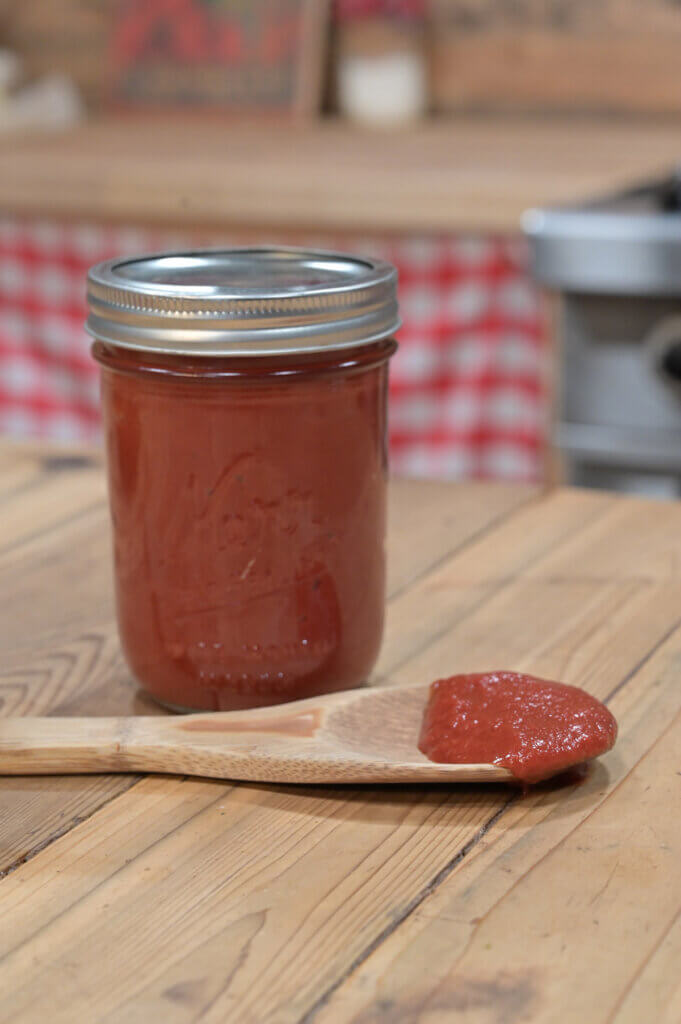 Jar of ketchup with a wooden spoon with ketchup on it.