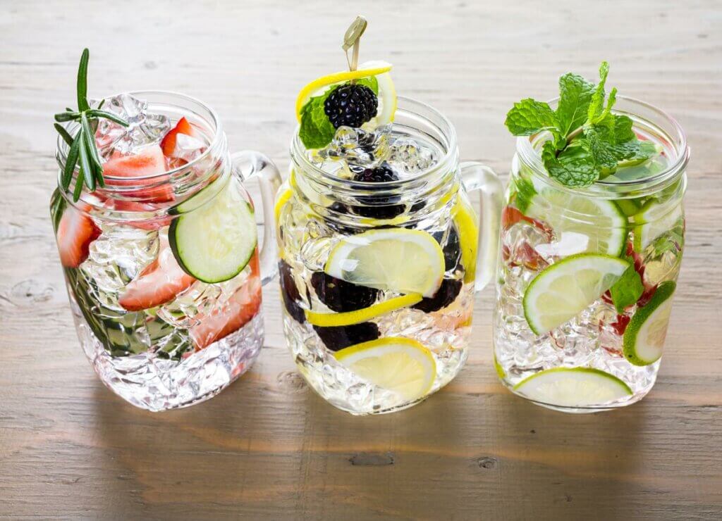 Three mason jar glasses filled with water and fruit and herbs for flavored water.
