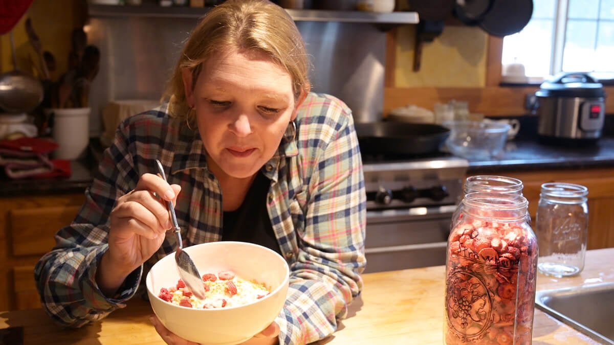 A woman taking a bite of yogurt with freeze dried strawberries on top.