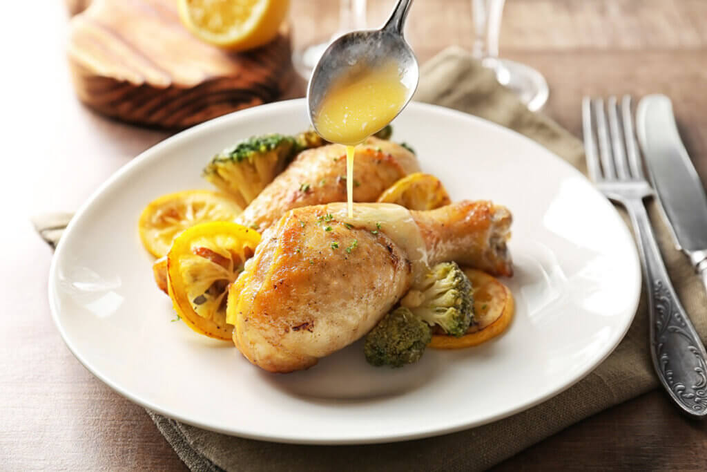 Chicken served on a plate with lemon sauce being drizzled over the chicken.