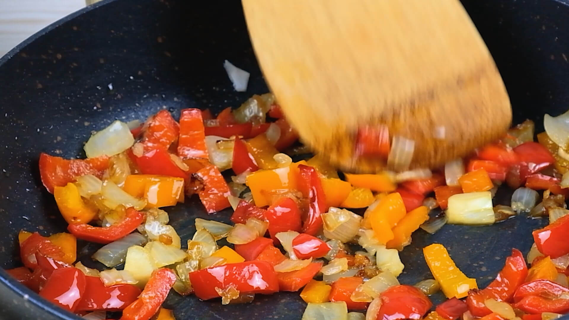 A spatula stirring peppers and onions sauteing in a cast iron skillet.
