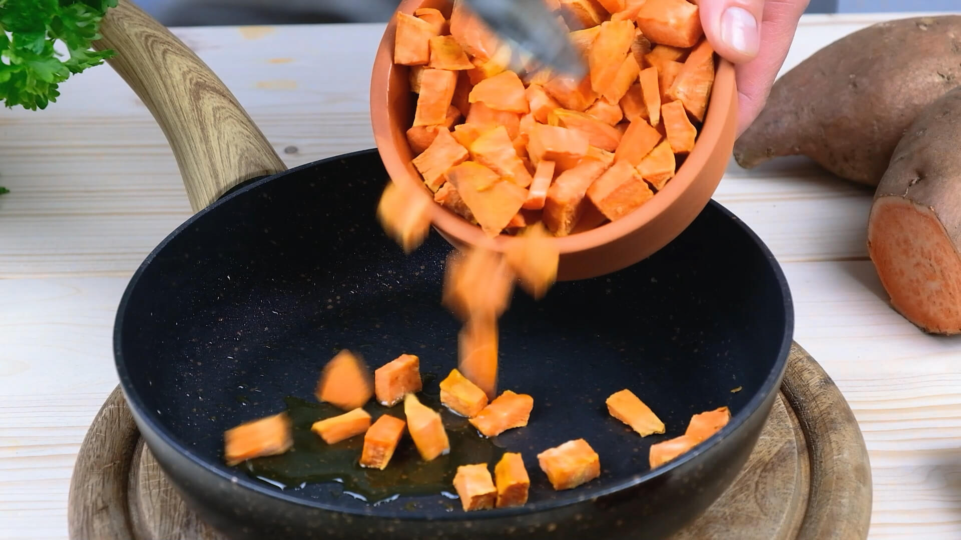 Pouring sweet potatoes from a bowl into a greased cast iron skillet.