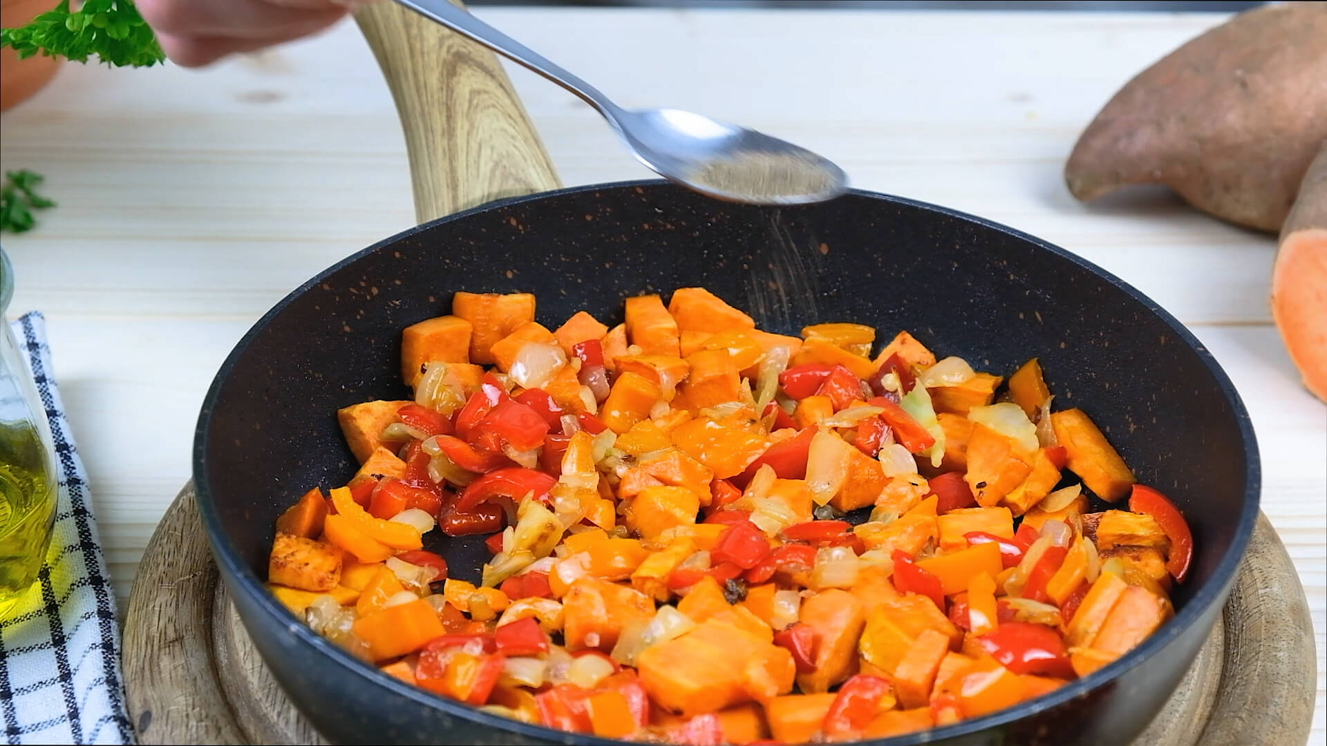 Sprinkling sweet potato hash in a cast iron skillet with ground black pepper.