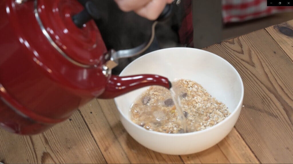 Pouring boiling water from a red tea kettle into a bowl of instant breakfast.