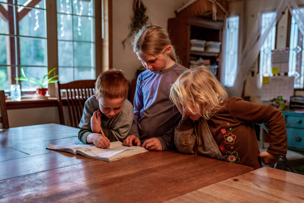 A young girl helping her younger siblings with school work.